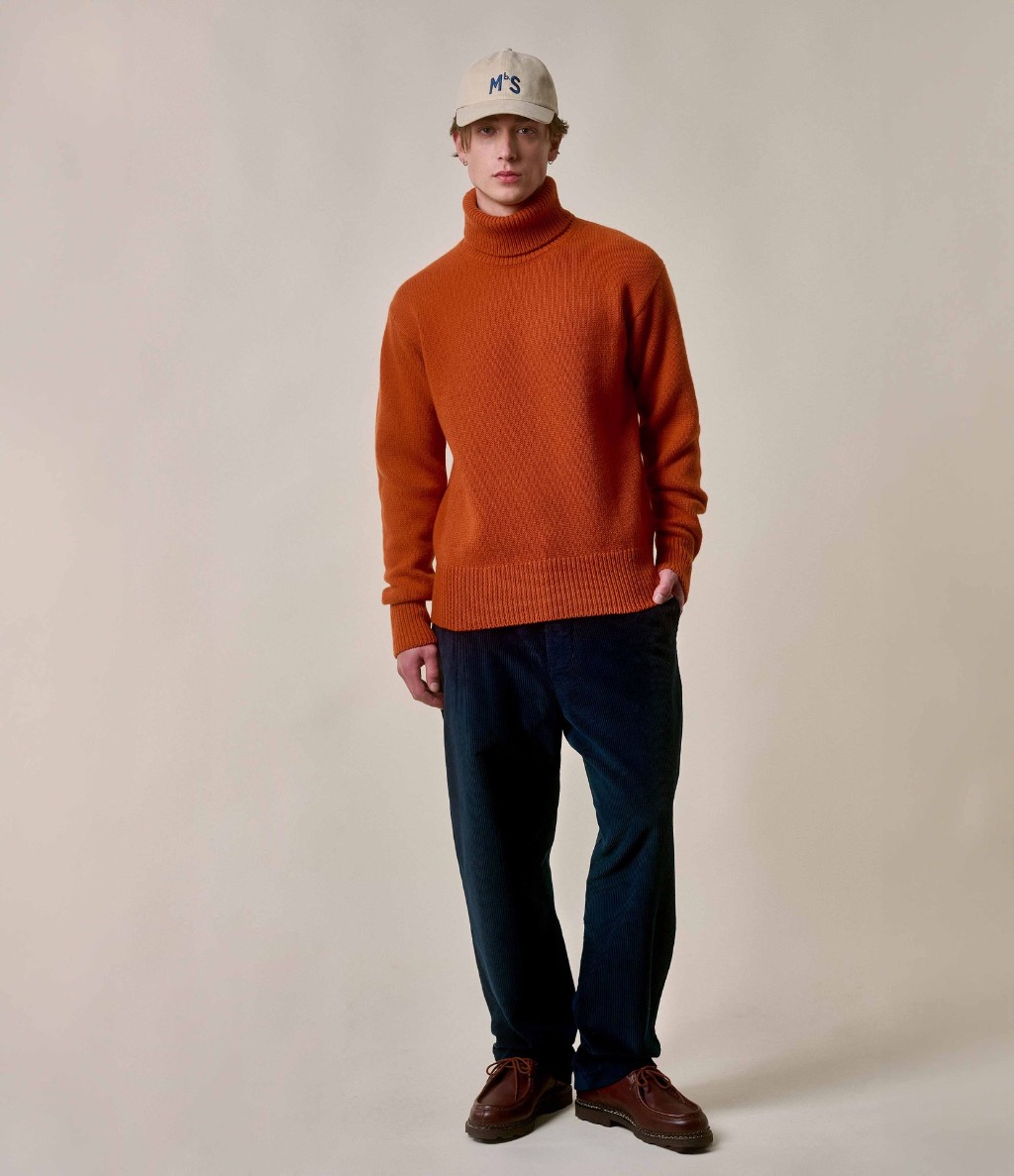 Man wearing orange turtleneck pullover and blue corduroy chinos