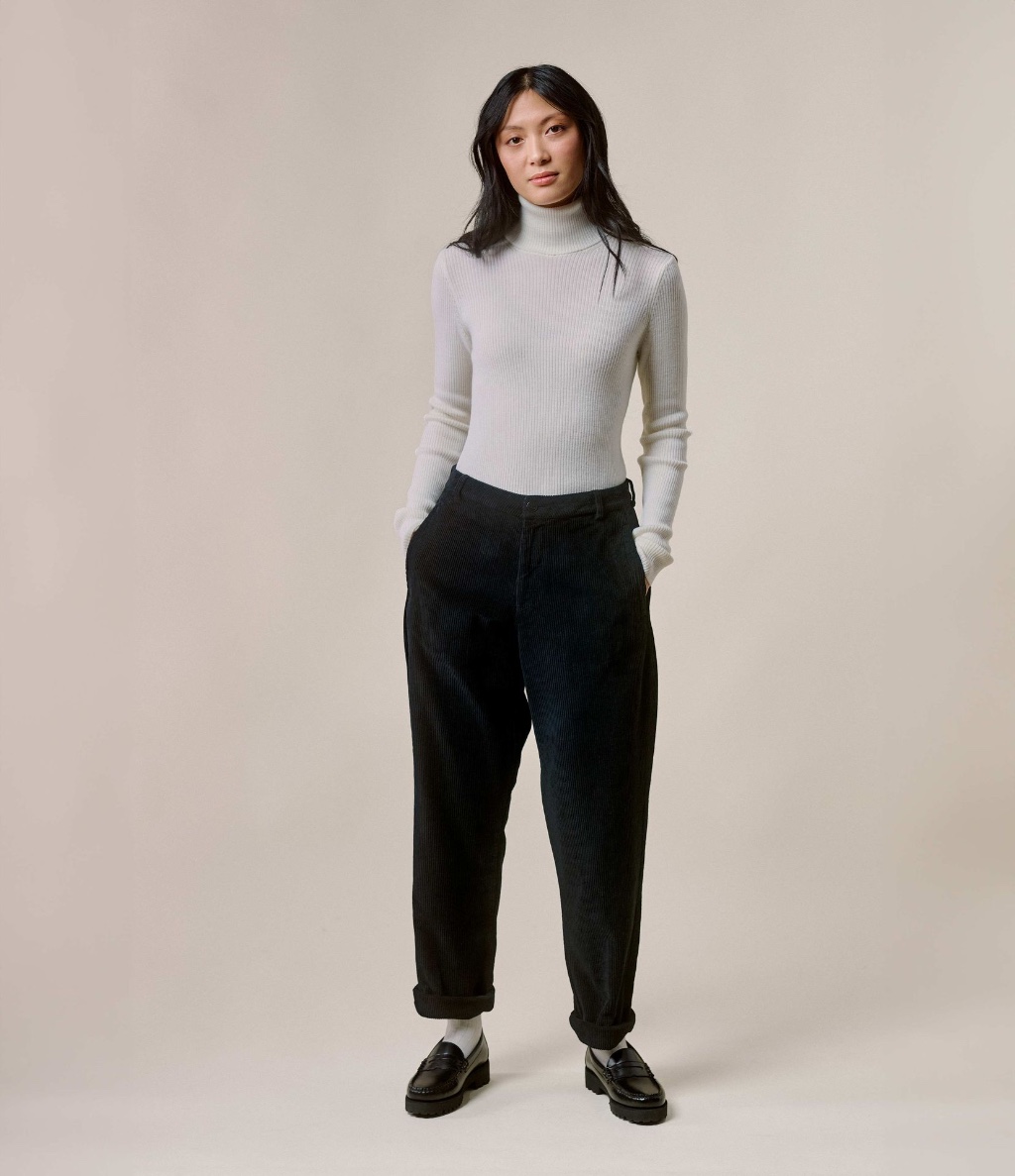 Woman wearing ecru turtleneck pullover and black corduroy chinos
