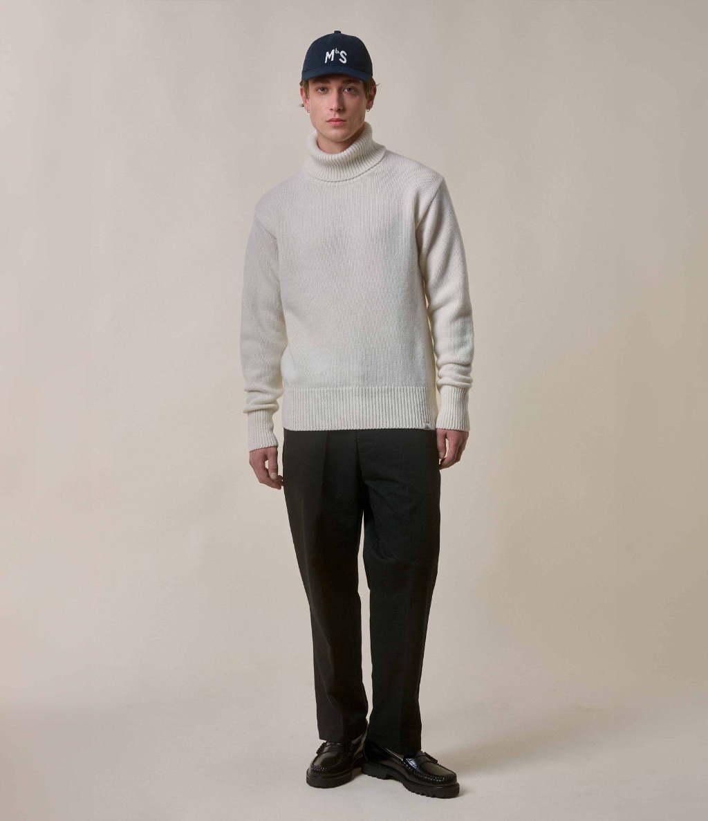 Man wearing ecru turtleneck pullover and black twill chinos