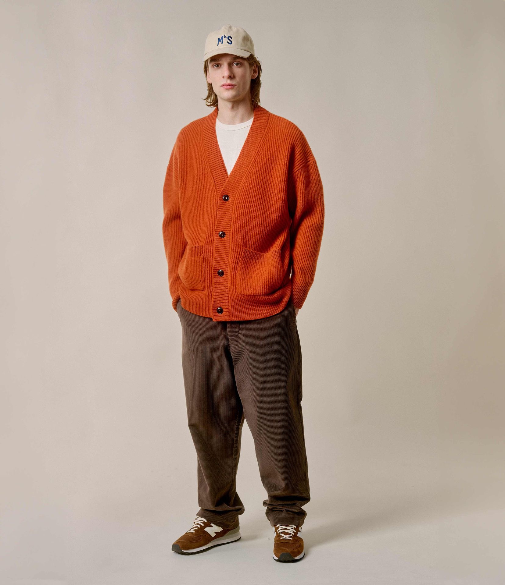 Man wearing orange knit cardigan and brown corduroy chinos