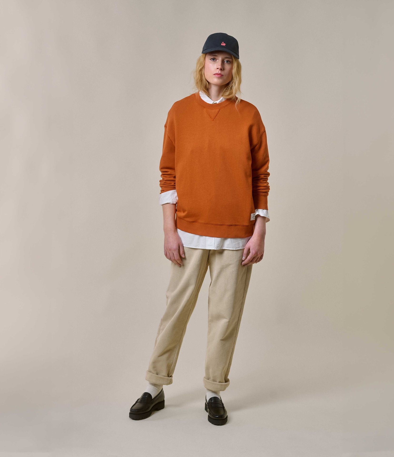 Woman wearing orange crewneck sweatshirt and ecru corduroy chinos