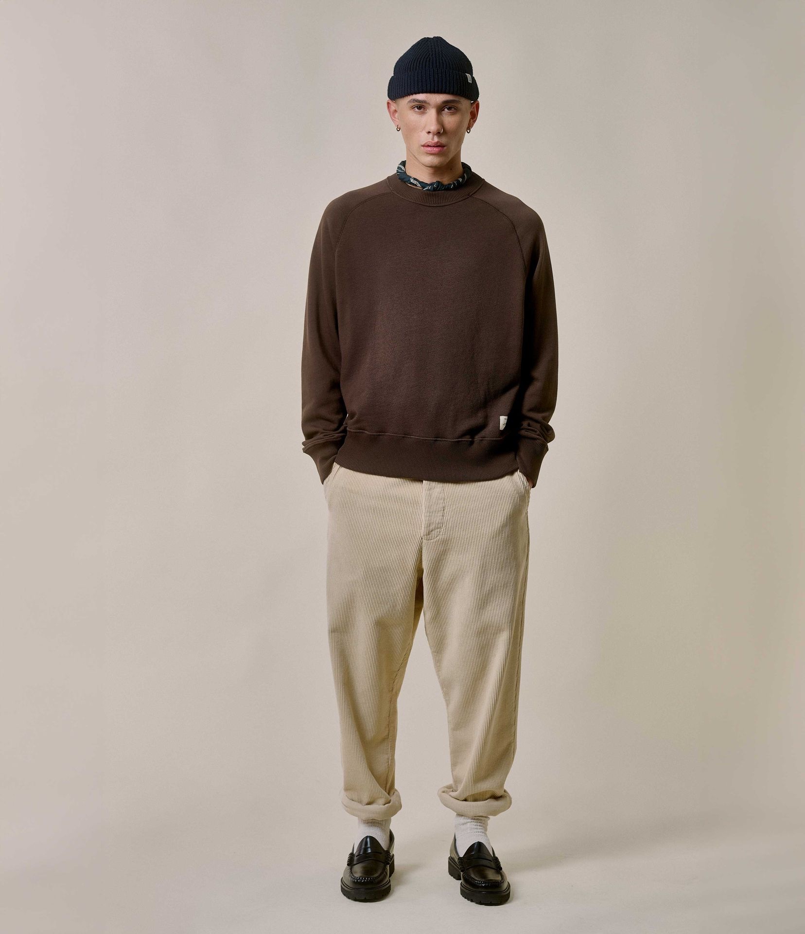 Man wearing brown crewneck sweatshirt and ecru corduroy chinos