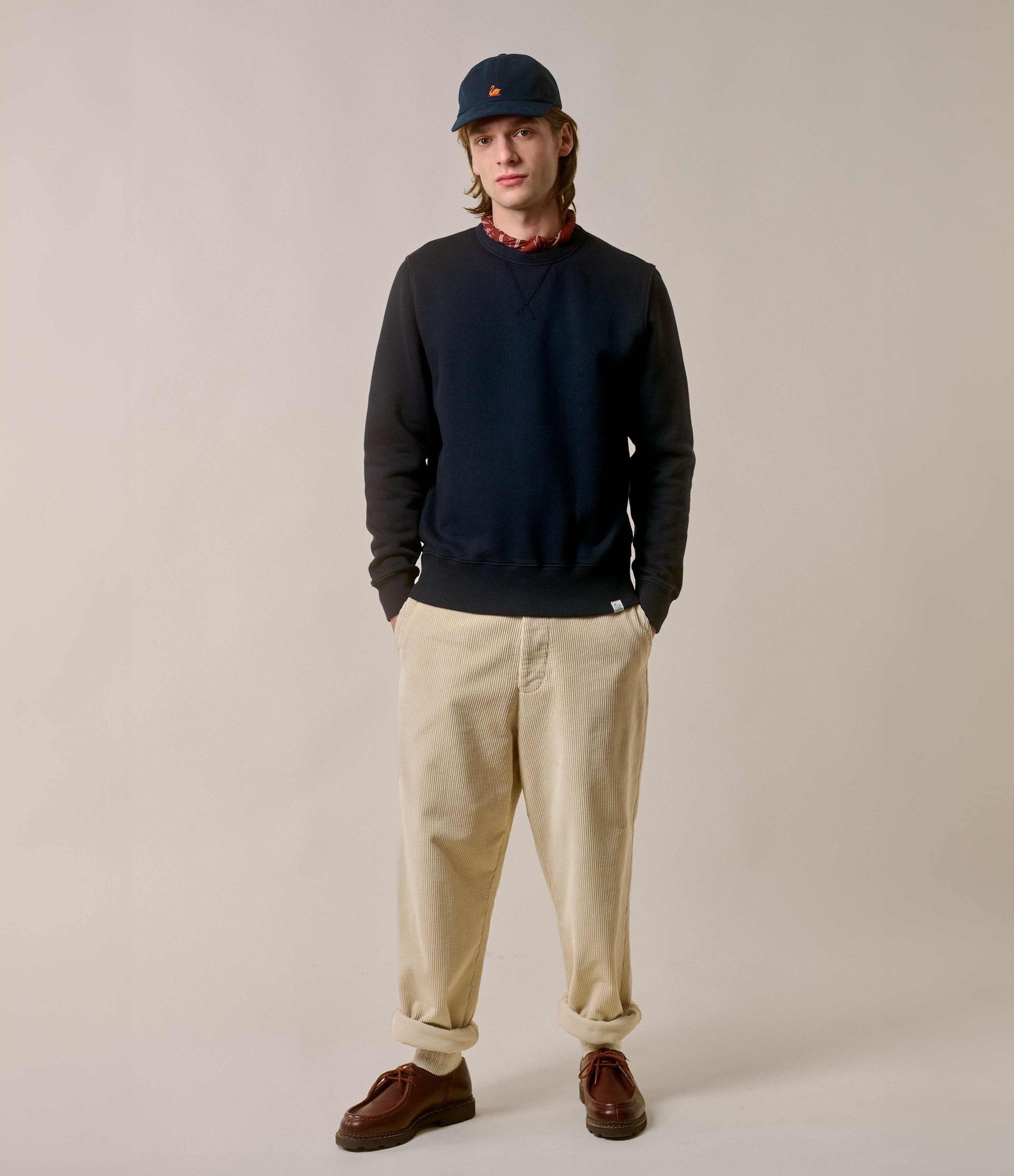 Man wearing navy crewneck sweatshirt and ecru corduroy chinos