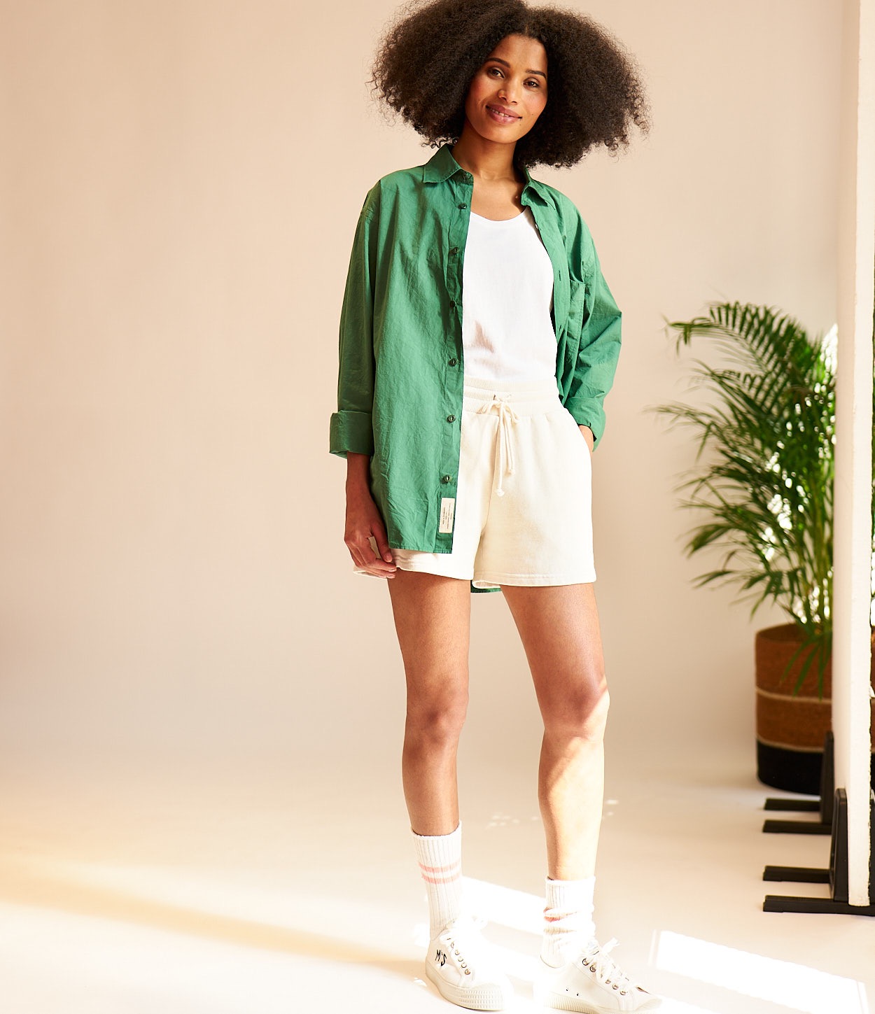woman wearing green poplin shirt, sweat shorts, socks and novesta sneakers