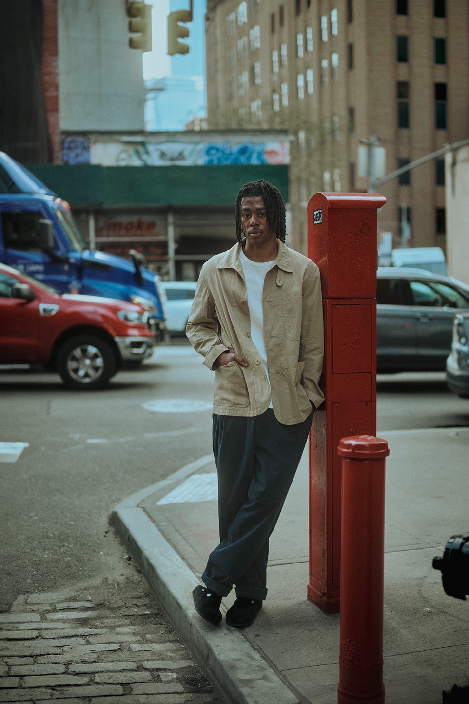 man resting on a phone booth wearing white t-shirt, jacket and pants